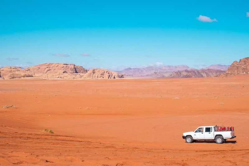 Find out what to wear in Wadi Rum, white truck driving through the desert under a clear blue sky