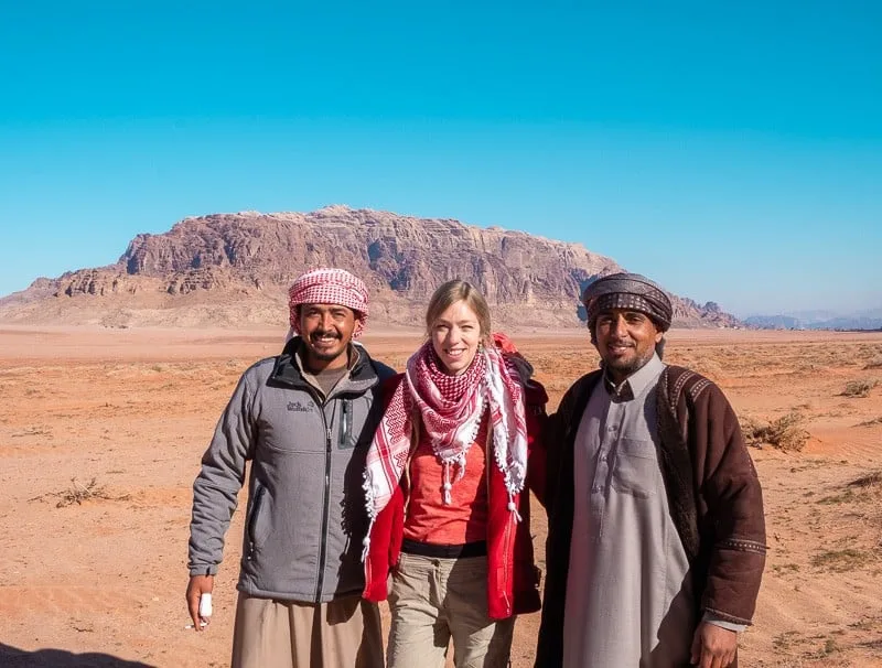 Don't forget to take some Wadi Rum bedouin camp photos, Paulina standing With Hussein and Mohammed from Wadi Rum Quiet Village with large rocky mountain behind under a bright blue sky