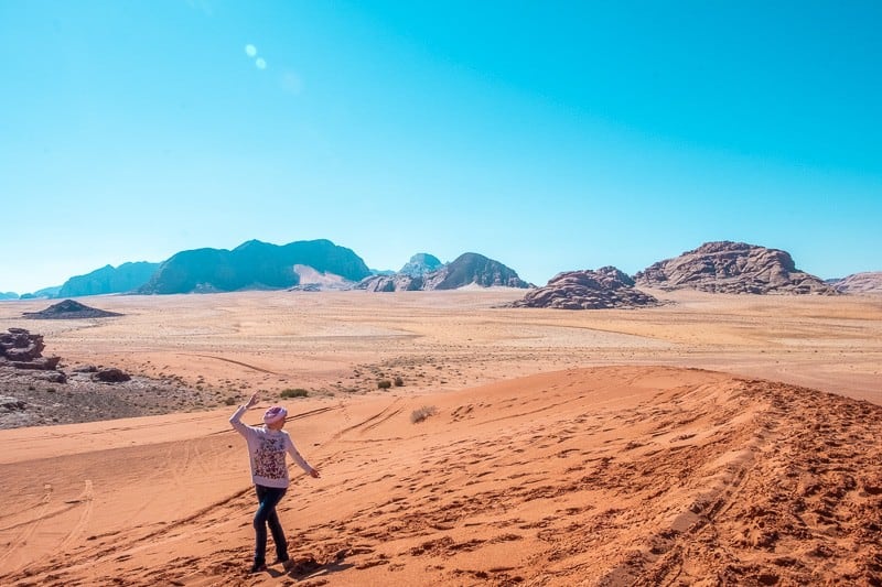 Try out some of these things to do in Wadi Rum for couples, person walking through sand with wide vista of desert and rock formations behind