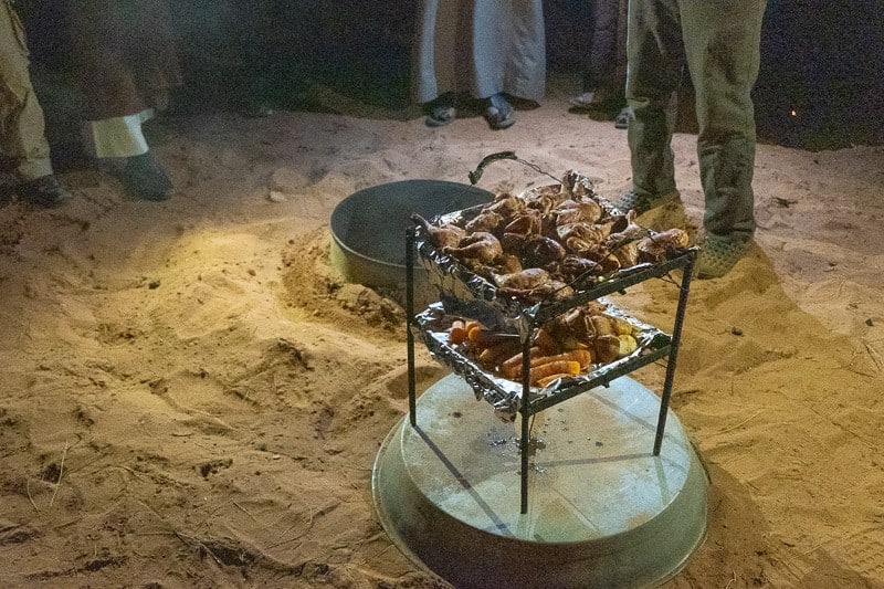 Learn about what can you do in Wadi Rum, tiers of cooked meat standing on a metal tray sitting in the sand