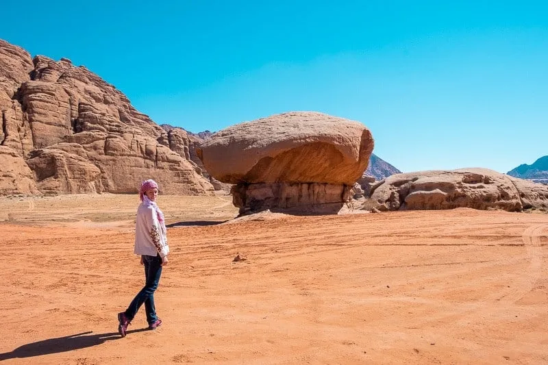Don't forget your best Wadi Rum outfit, person standing in front of The Mushroom Rock under a bright blue sky