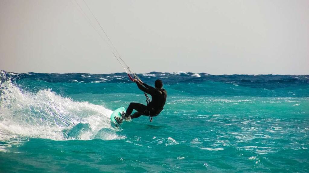 Get into some of the Best Things to do in Boa Vista, person in wetsuit on surfboard holding onto the reins of a parachute as they slide along the surface of the sea