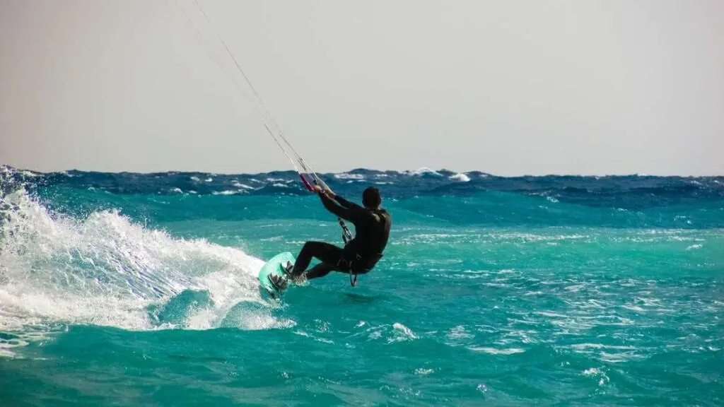Get into some of the Best Things to do in Boa Vista, person in wetsuit on surfboard holding onto the reins of a parachute as they slide along the surface of the sea