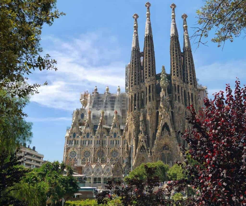 a facade of Sagrada Familia church from a frame with plants on a bright day