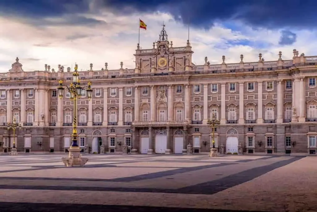 Discover the wonders of the paradores of spain this year, view of large palatial building with mand columns and stone arches with large stone courtyard in front