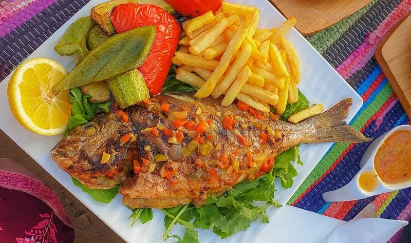 cooked fish with lemon, fries, and vegetables on a plate, things to do in aqaba, jordan, red sea, wadi rum day trip, petra day tour, resorts, ayla oasis, souk, shopping, egypt, beaches, luxury, snorkeling, diving