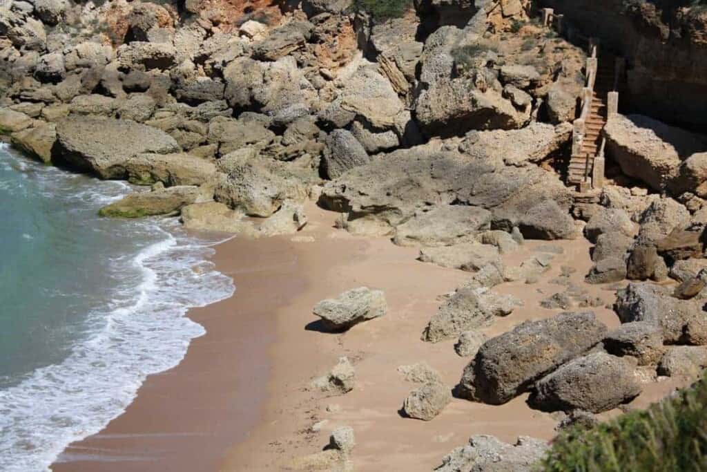 a beach filled with big rocks with a small pathway with waves crashing on the beach