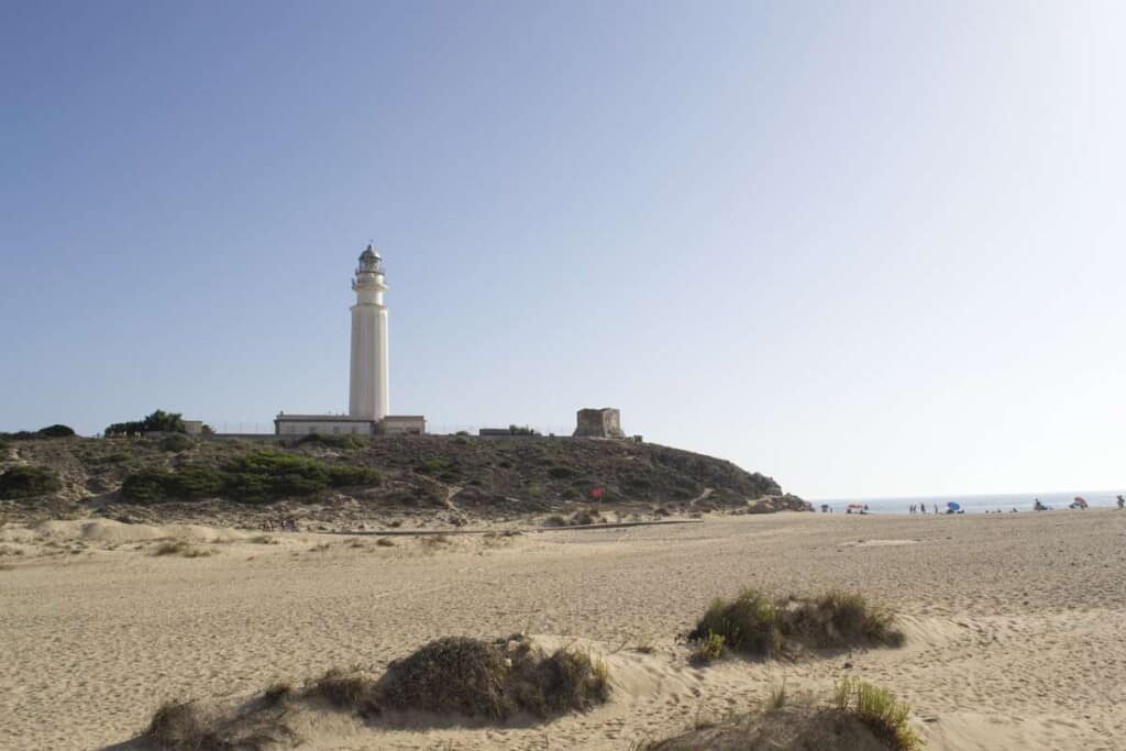 lighthouse on a hill with grass and moss by the beach with people far away by the sea