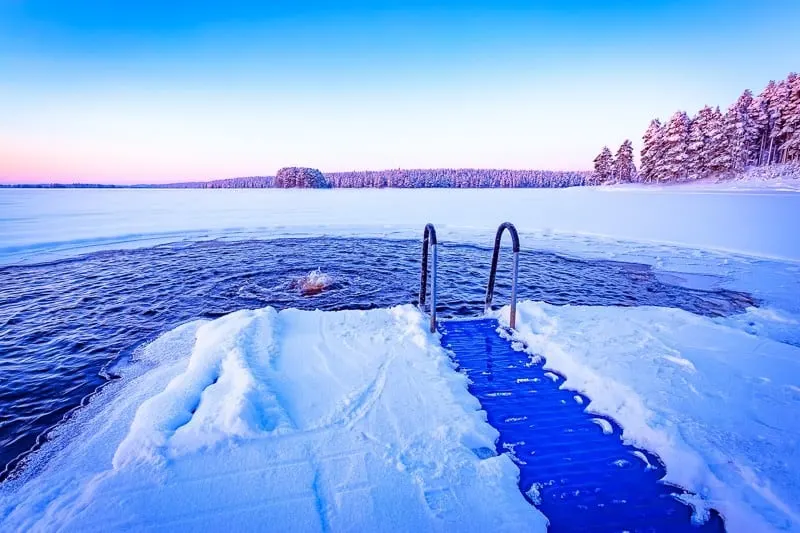 best things to do in Wisconsin Dells in winter, view of short pathway leading to steps into an outdoor pool at the edge of a vast frozen lake surrounded by trees all covered in a layer of snow