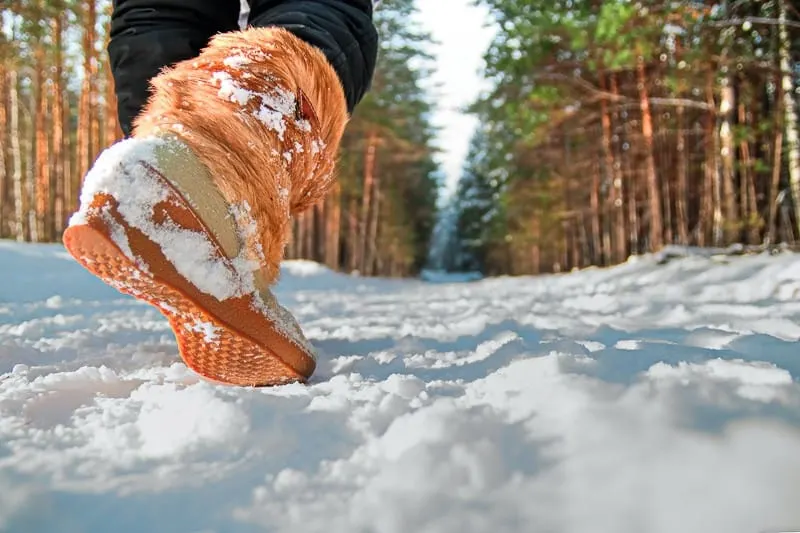 Leg woman in winter shoes walking on the snow in a winter park. Closeup outsole of warm boot.