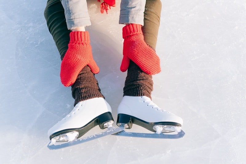 best things to do in lake geneva in winter, young girl with mittens in ice skates sitting on ice and leaning forward