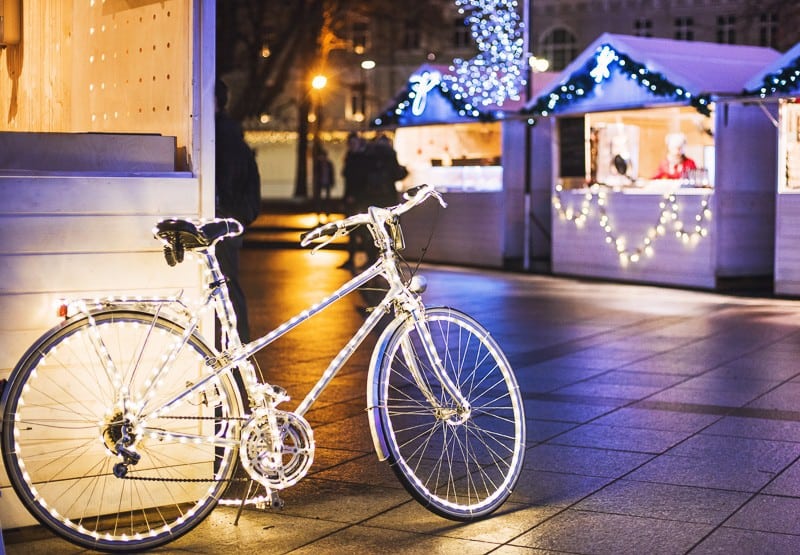 a bike with white lights parked on a side walk with christmas market shops at the background, Traditional Christmas market in Europe