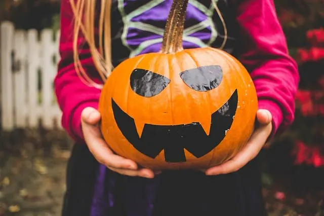 fall things to do in milwaukee with family, girl holding a pumpkin with a face put on with black sticker