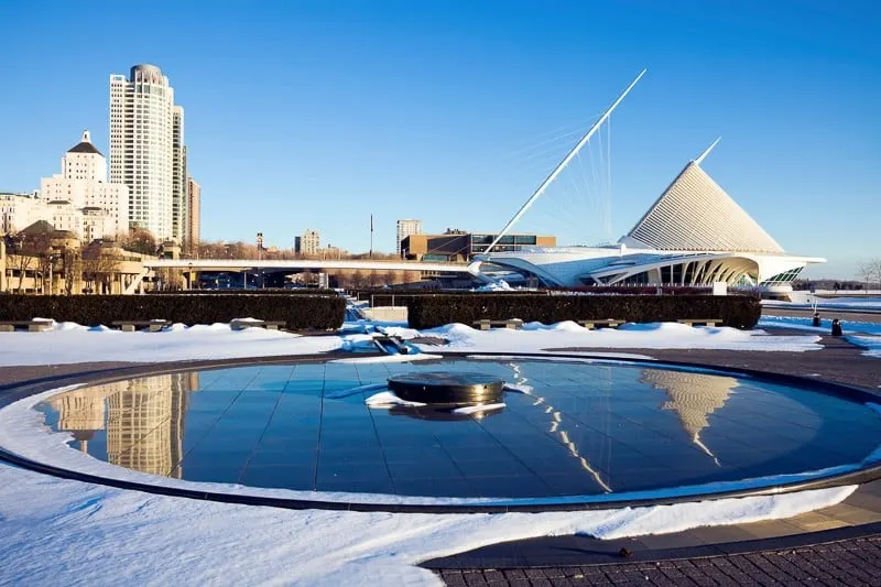 places to visit in winter in Wisconsin, large outdoor circular fountain with modern buildings and tower blocks behind all covered in a layer of snow under a clear blue sky