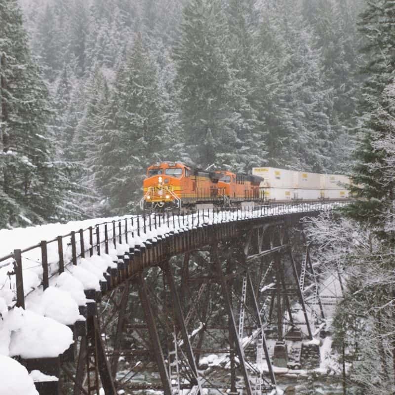 Lake Geneva in the winter, orange train driving over metal bridge in the snow surrounded by snow covered pine trees