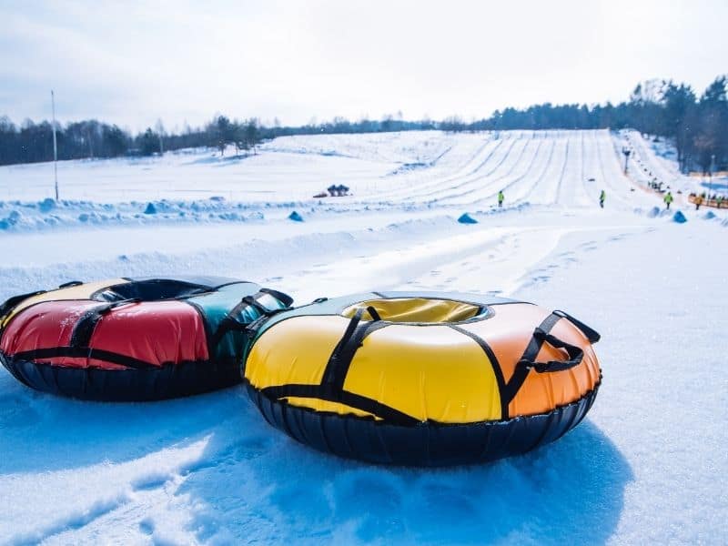 family-friendly vacations Wisconsin in winter, two snow tubes up close on snow with snow-covered hill and several people tubing in background