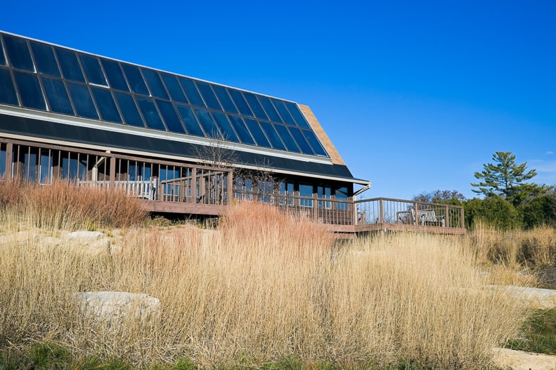 Discover the best places to visit in the fall in Wisconsin, view of Arboretum in Madison, University Of Wisconsin with large rooftop covered in solar panels sitting among some tall brown grass under a clear azure blue sky