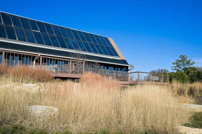 view of Arboretum in Madison, University Of Wisconsin with large rooftop covered in solar panels sitting among some tall brown grass under a clear azure blue sky