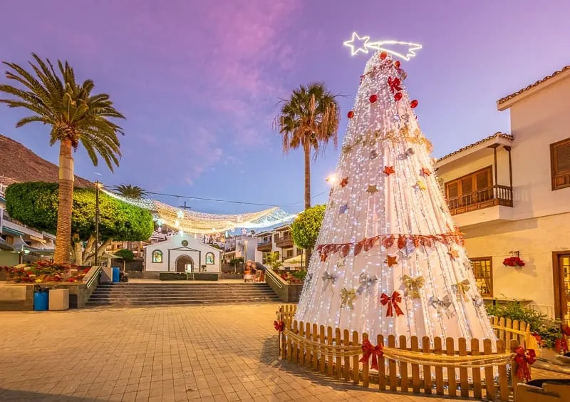 Town center with Christmas market at dusk under blue and purple sky with palmtrees and mountains in background