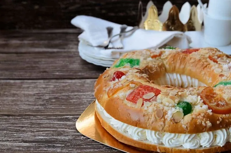 Roscon de reyes, kings' ring typical dessert eaten in Spain to celebrate Epiphany or Dia de Reyes Magos (Three Kings' Day). Spanish Christmas cake with fruits nut and icing on wooden background