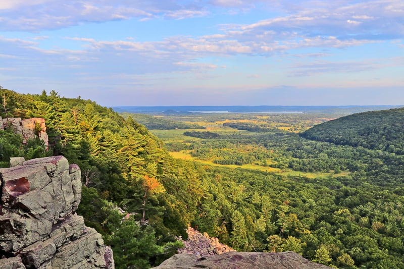See the best fall vacation spots in wisconsin for families, Areal view of wide valley full of lush green and yellow trees from rocky ice age hiking trail during sunset hours