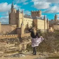 a woman posing and looking at a castle on the back, day trip from madrid to segovia, madrid day trip to segovia, segovia day trip, how to et form madrid to segovia, segovia itinerary