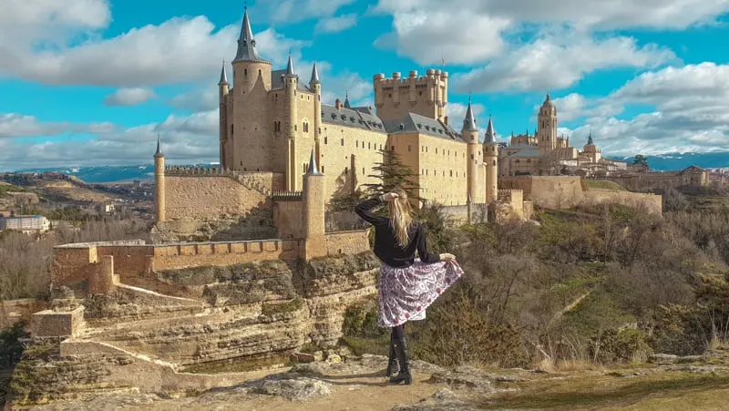 a woman posing and looking at a castle on the back, day trip from madrid to segovia, madrid day trip to segovia, segovia day trip, how to et form madrid to segovia, segovia itinerary