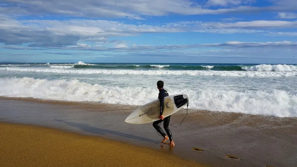 surfing in spain, man walking on the beach with surf gear