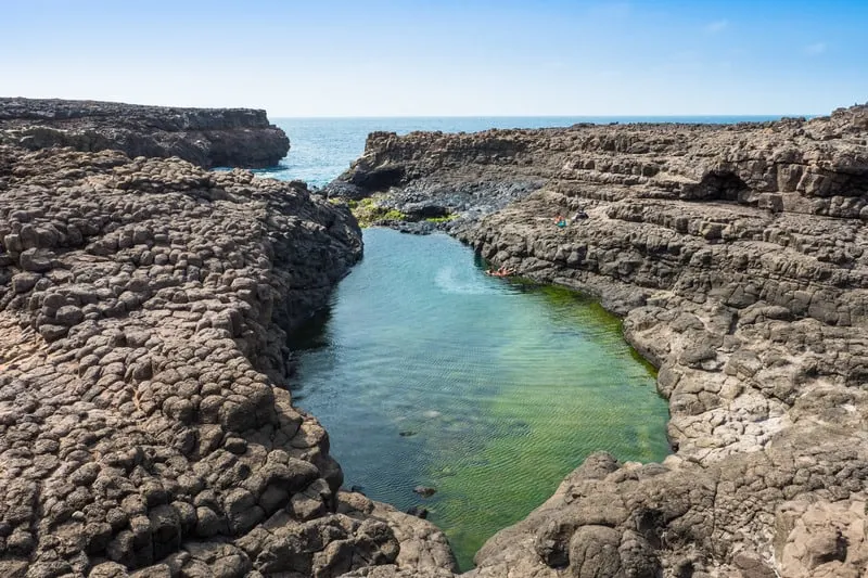 a picture of Buracona in Sal Island filled with rocks and a small body of water in the middle connected to the sea