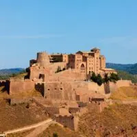 Check out these movies set in Spain, view of tall fortified stone structure with many tall buildings clustered together behind a large wall on top of a hill