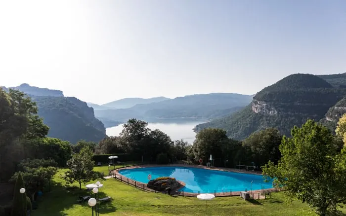 Don't miss any of these breathtaking spanish government hotels, view of outdoor swimming pool surrounded by neat green lawn with trees and bushes in front of a wide vista of a lake banked by tall green hills