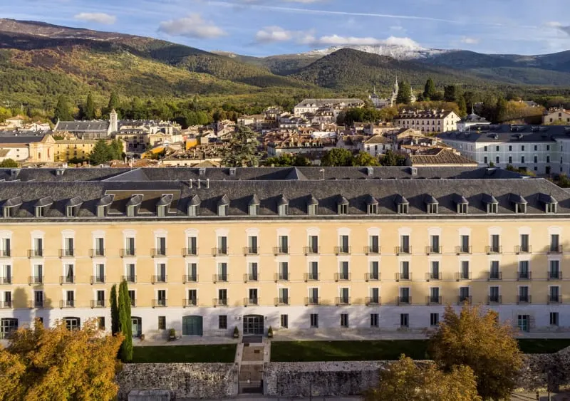 Learn some history at some of the oldest hotels in spain, view of large building with dozens of neatly spaced windows in front of a skyline of older residential buildings and rolling green hills