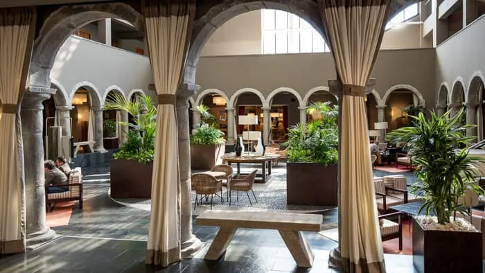 Discover your new favorite government hotels in spain, hotel interior with central seating area surrounded by walls with arched doorways and long curtains as well as green plants in flowerbeds throughout