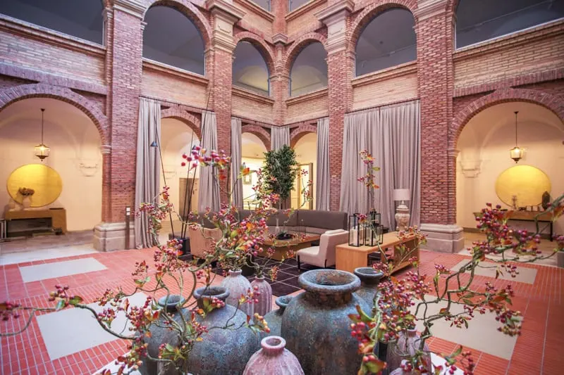 Enjoy the best paradores in Spain this year, hotel interior with ornate tiled pillars and floors covered in bespoke furniture and flower pots with budding flowers