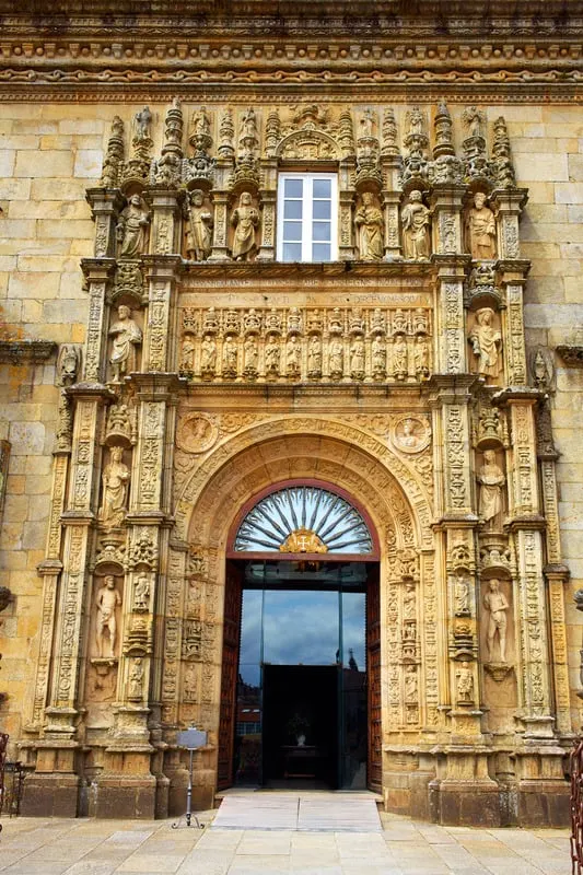 Make use of a detailed map of paradores in spain, ornate stone doorway with elaborately carved small statues arranged in neat rows and columns with each under their own individual arches