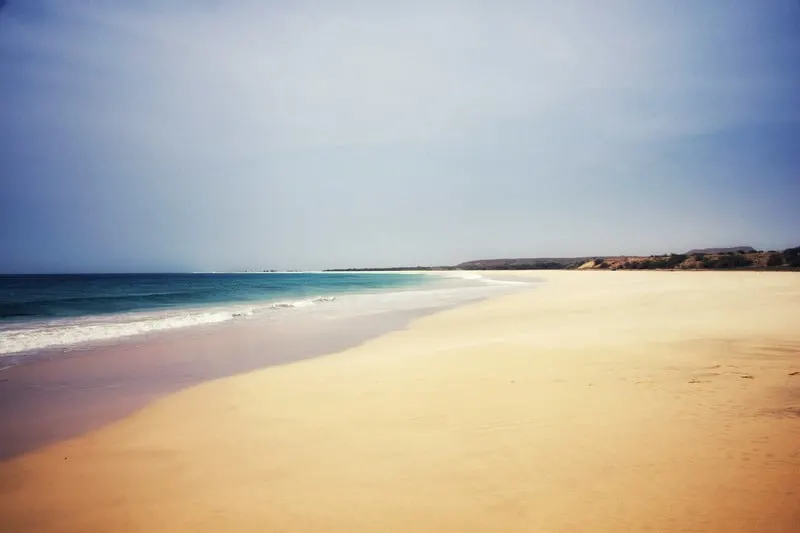 Try out some things to do in cape verde boa vista, view of long empty beach with golden yellow sand and deep blue seawater to one side under a wide open sky
