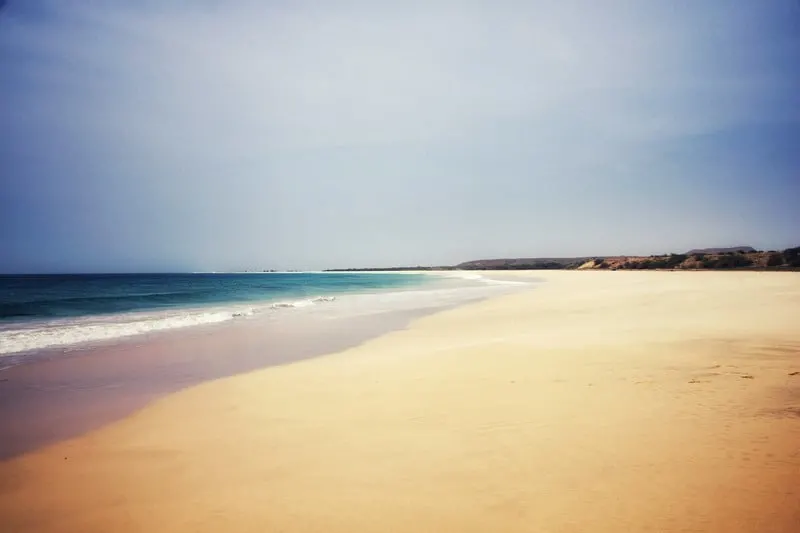 an empty beach with white sand and hills at the far end on a sunny day