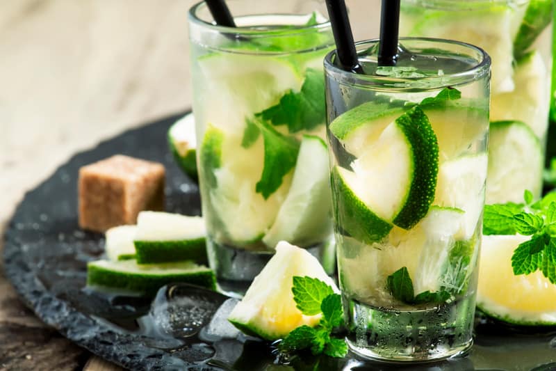 cocktail drinks with lime slices in glasses with straw on a black plate with lime slices and ice