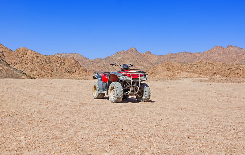 Discover what is there to do in cape verde, unattended quadbike sitting on an open patch of sand in front of a plethora of rocky sandy hills under a clear azure sky