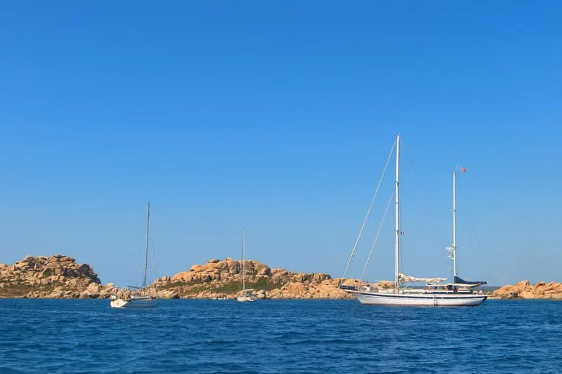 Don't miss out on the day trips from boa vista to sal, view across the water of several sailing boats moored next to a peninsula of rocky ground under a clear blue sky