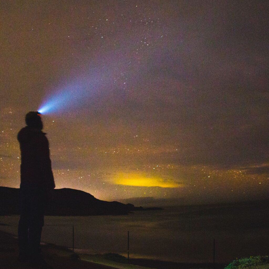 a man with a headflashlight stargazing on by the beach during the night