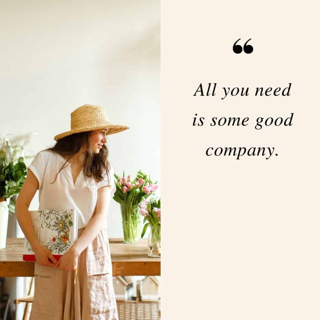 All you need is some good company; a woman wearing a straw hat and carryingg a book looking at flowers on a vase on her side