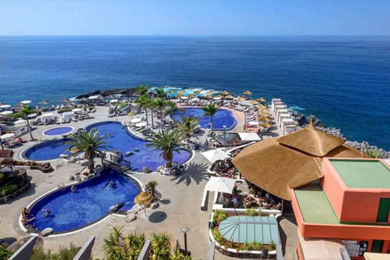 Stay at the best Tenerife resorts for families, Best view of resort with its series of carefully arranged swimming pools surrounded by green palm trees and sun loungers with blue water behind