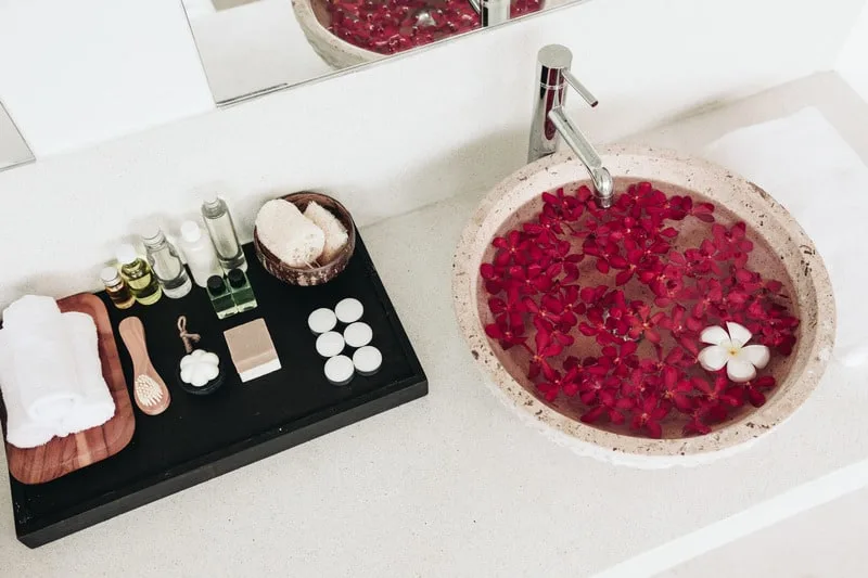 Staycation ideas for couples, Bathroom spa decoration with  bath oils and sink full of red flowers