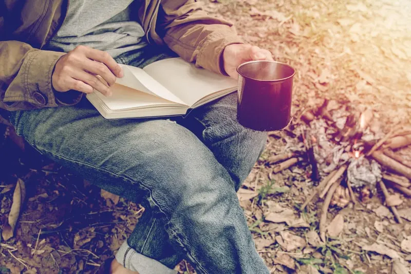 young man sitting is reading a book in outside the tent. Alone camping in forest.