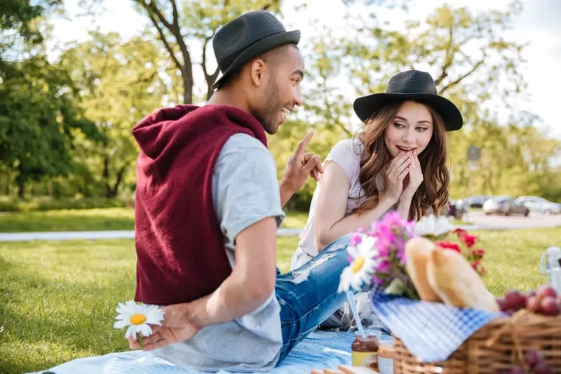 Staycation Ideas for Couples, Couple having picnic in park with some tasty finger foods and fruit.