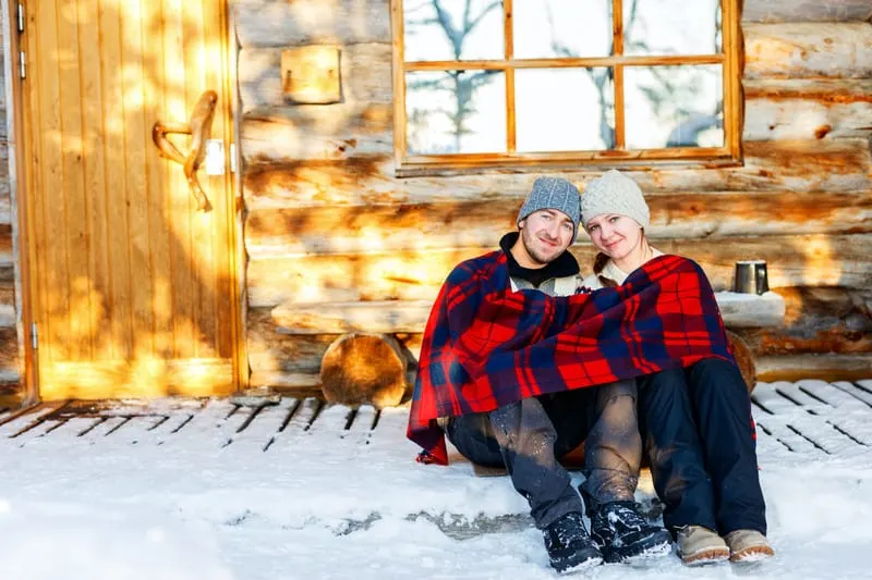 Go on a romantic weekend getaway to Wisconsin Dells, couple sat together om the snow beneath a blank outside of a cabin