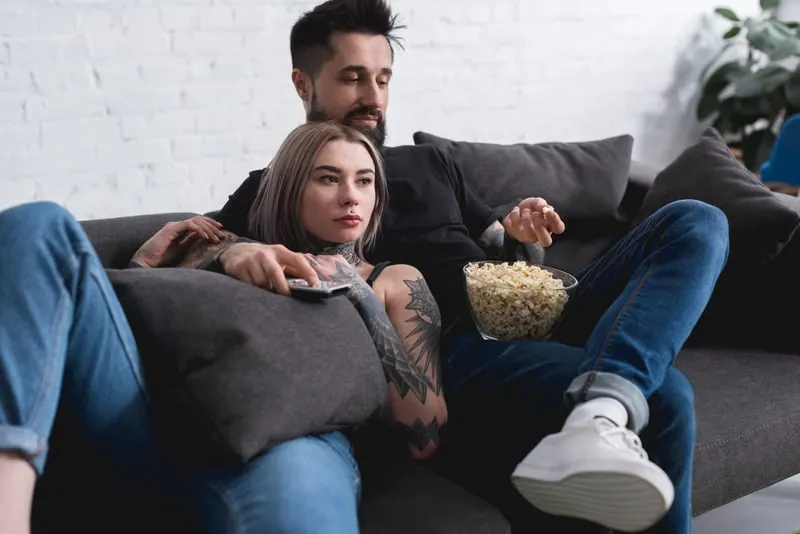 Try out some fun things to do in Wisconsin in October, couple sitting on dark couch with a bowl of popcorn as they watch television