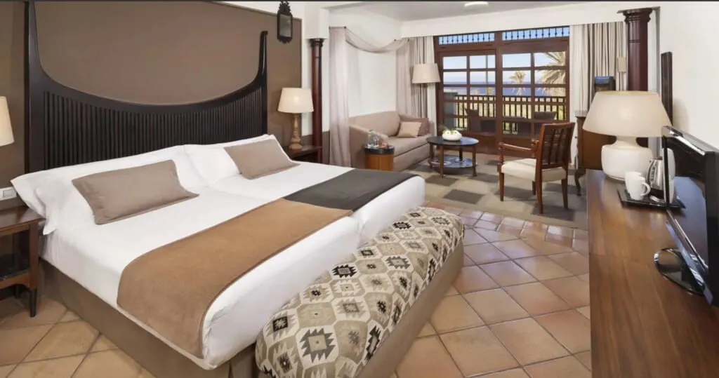 Check out these 5-star hotels in tenerife adults only all inclusive, interior of spacious hotel room with large bed and living room area with wooden chairs and sofa next to balcony