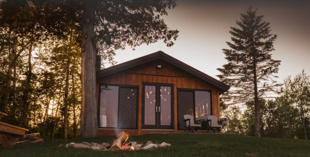 front of lake view cabin in Wisconsin with lit campfire in the foreground and tall trees to either side during sunset